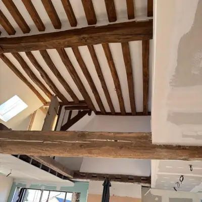 Poutres anciennes conservées et mises en valeur entre des plafonds neufs en plâtre