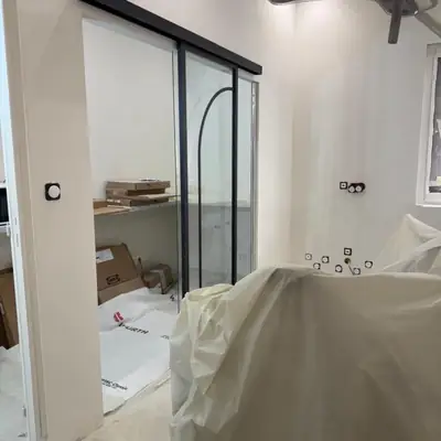 Cloison vitrée à châssis noir séparant deux pièces, chantier en cours de finition